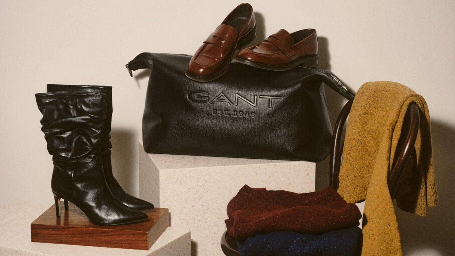 Black Gant bag with brown shoes, black boots, and a yellow scarf on a white background