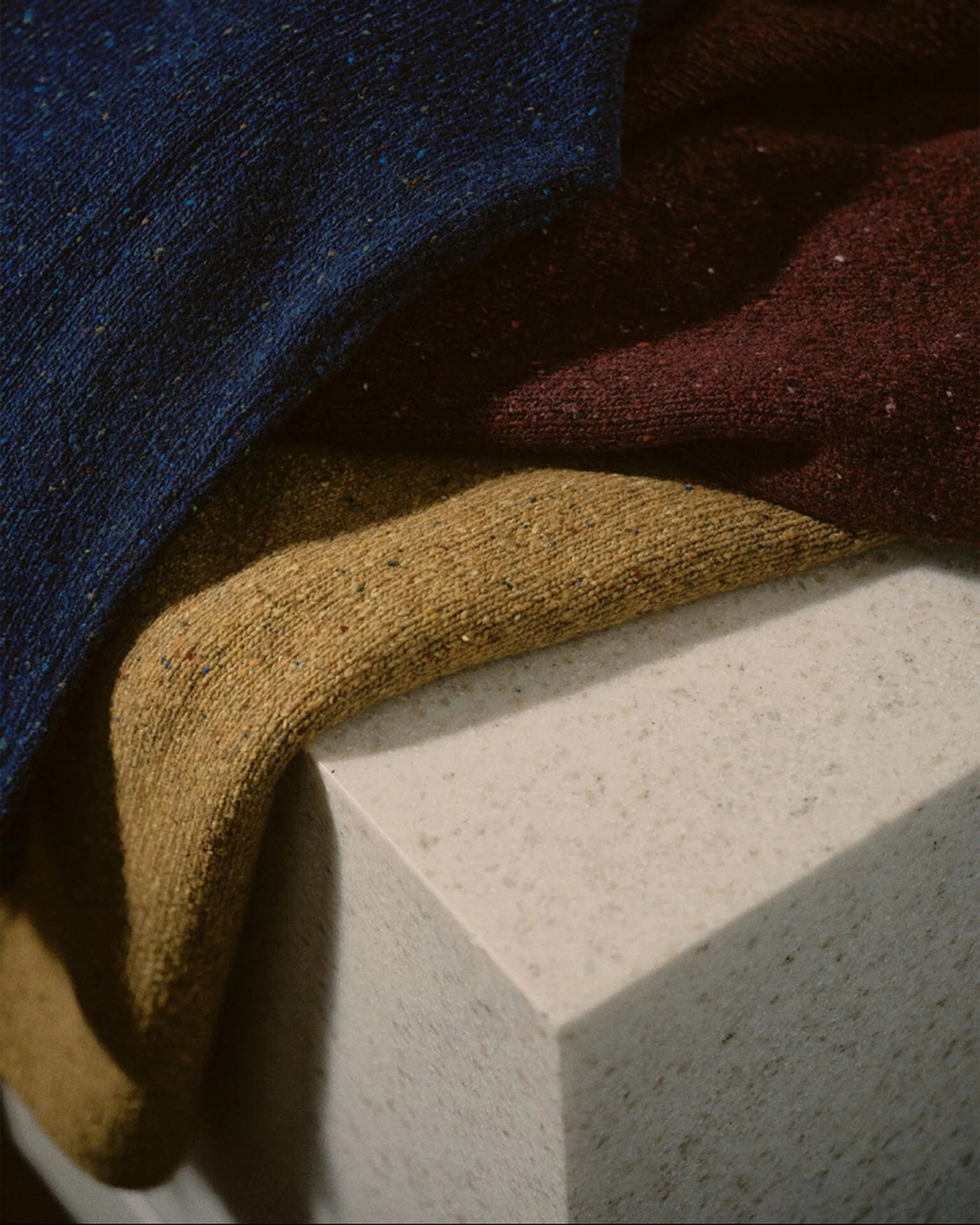 Close-up of textured fabric in blue, red, and gold on a concrete surface
