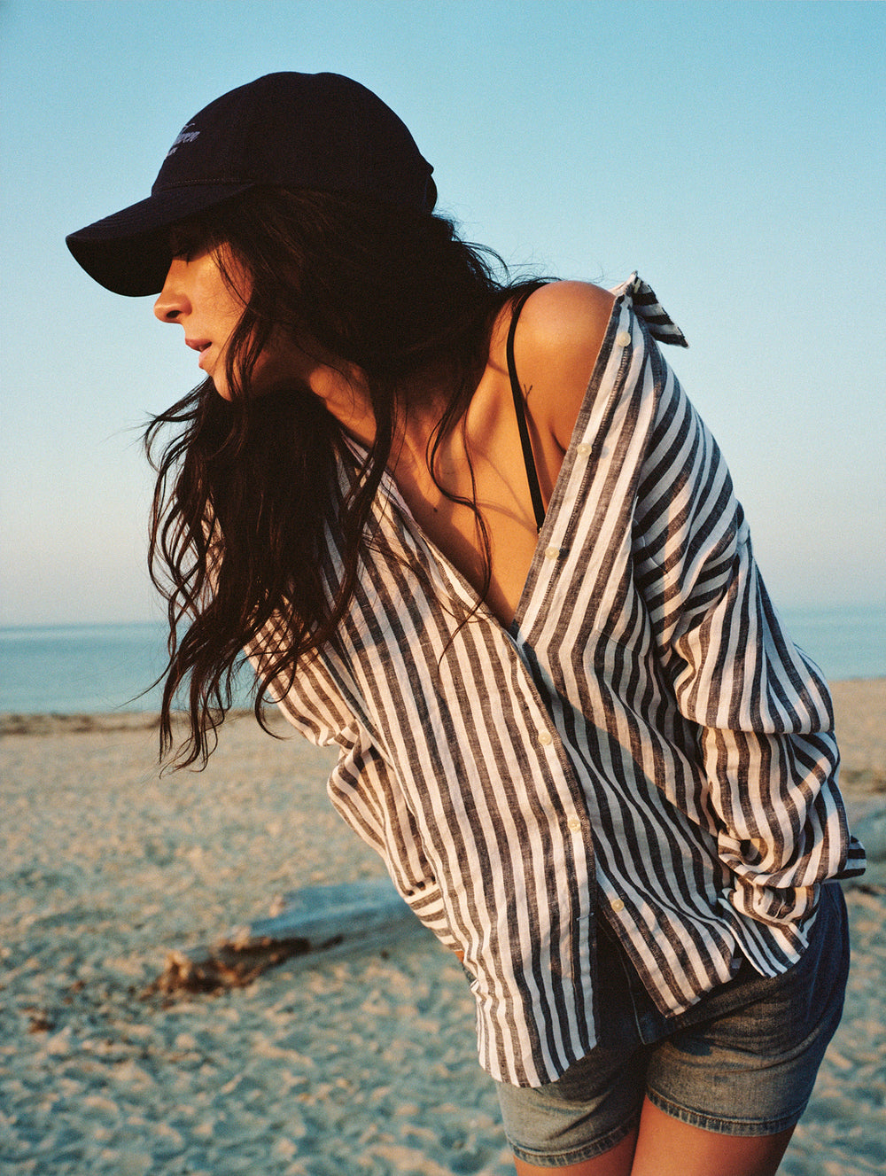 Woman on a beach wearing a GANT striped shirt and cap with ocean view