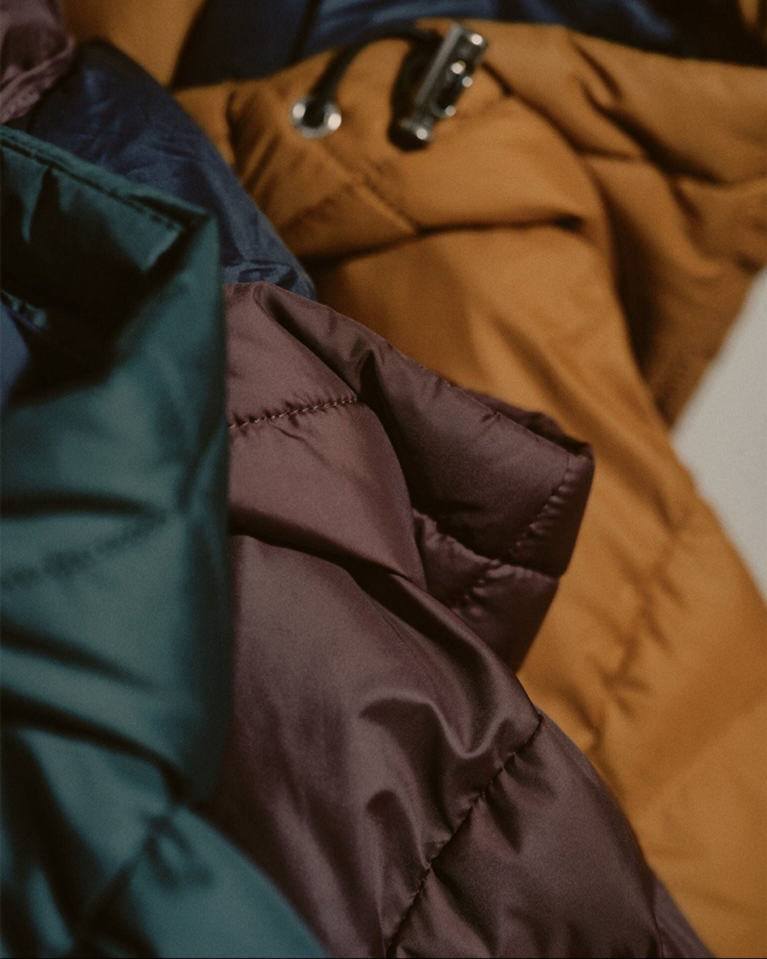 Close-up of folded winter jackets in various colors on a textured surface.