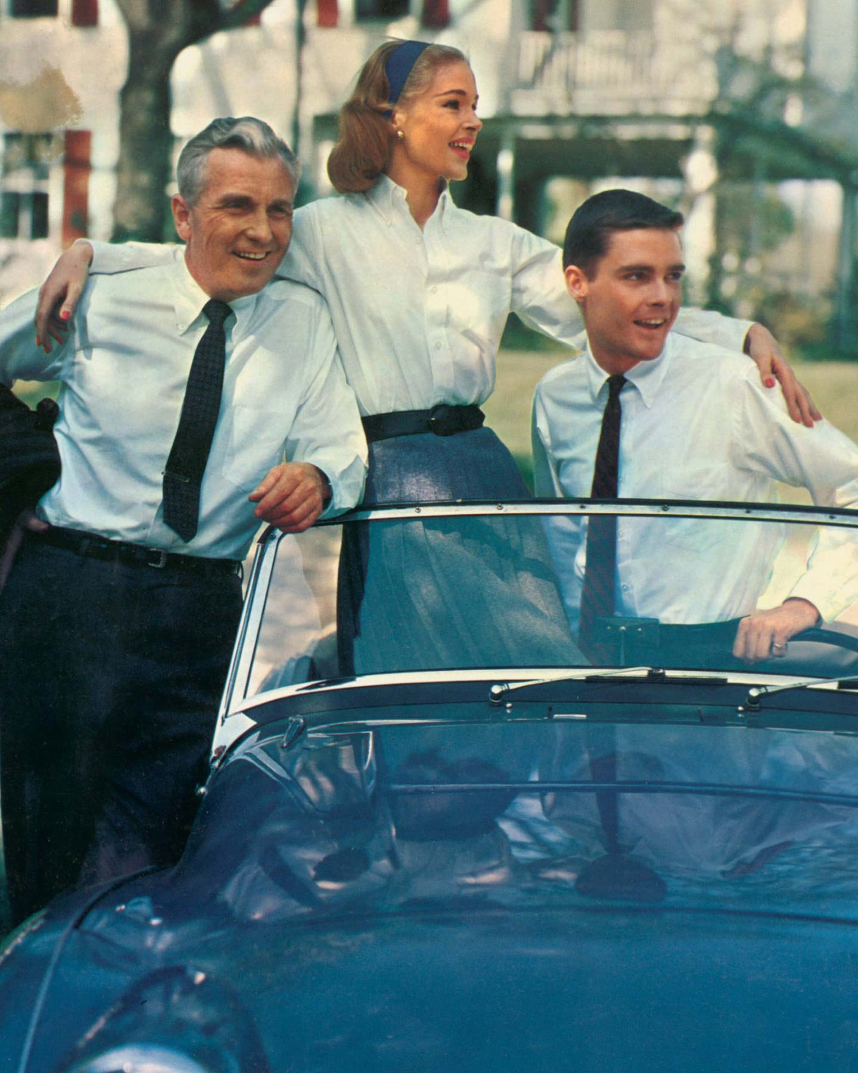 Three people in matching outfits standing next to a convertible car.