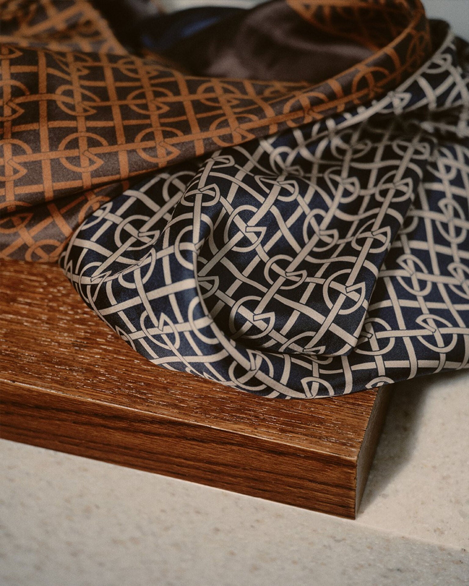 Two patterned scarves, one brown and one black and white, on a wooden surface.