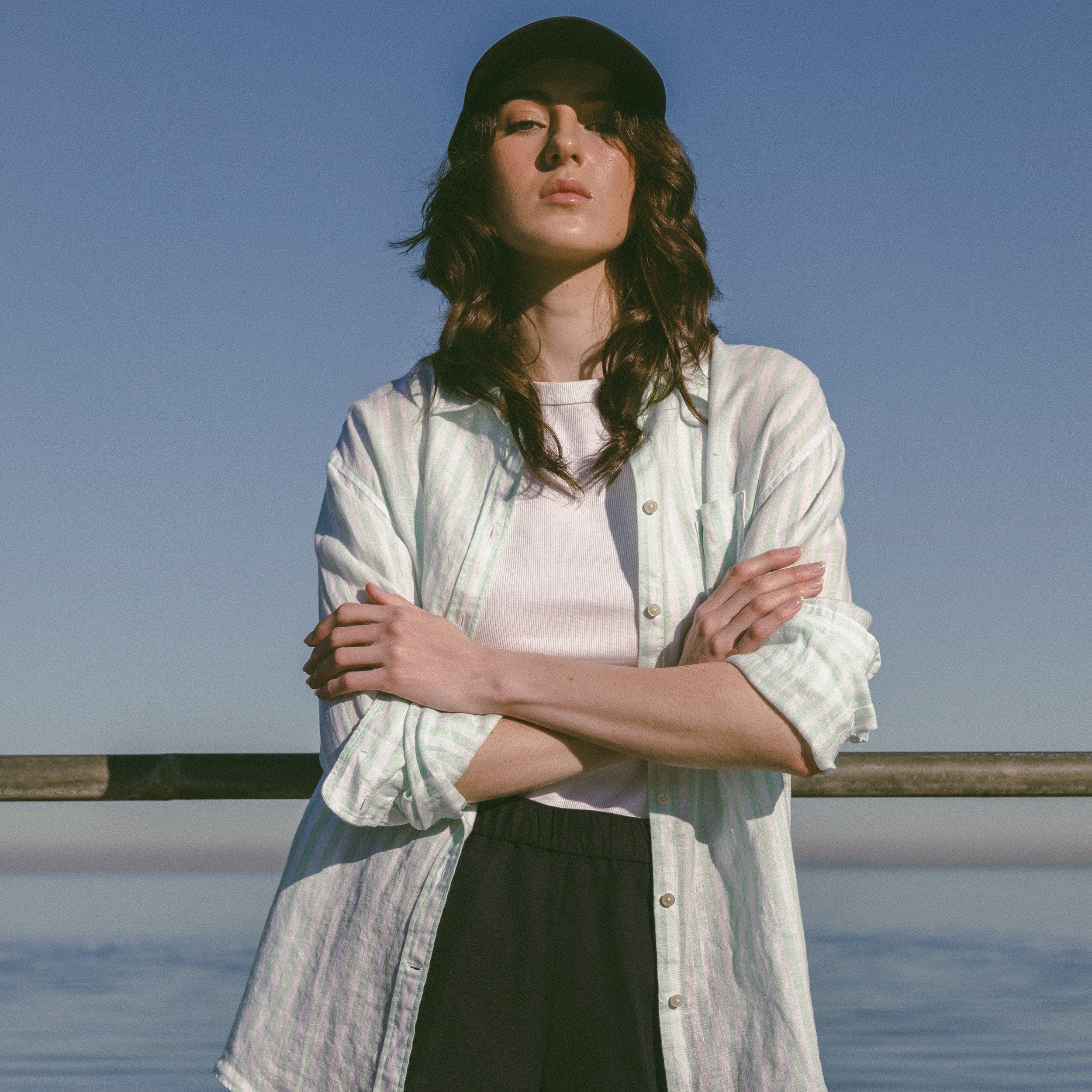 Woman standing by a body of water with a clear blue sky in a GANT linen shirt.