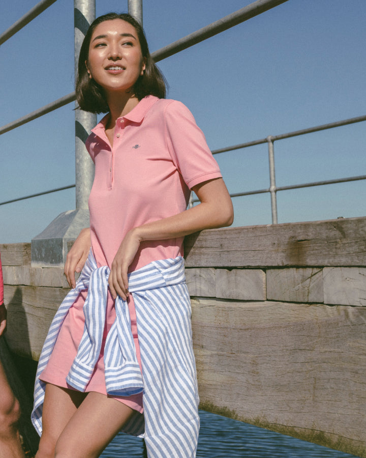 Woman wearing a pink polo shirt and striped skirt standing on a wooden dock.