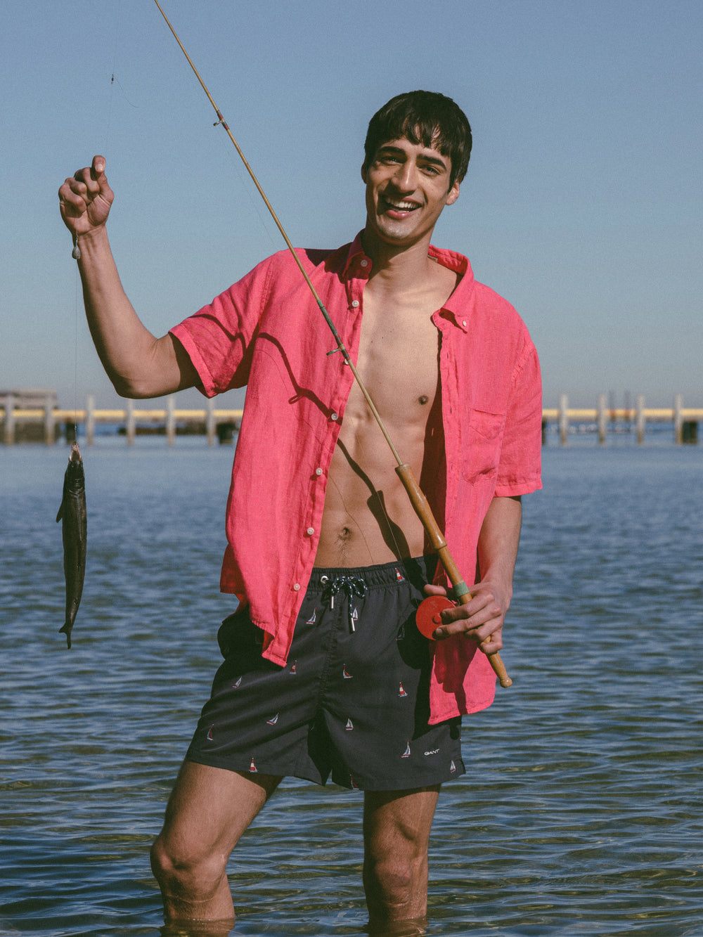 Man standing in the water holding a fishing rod, wearing the GANT Regular Fit Garment-Dyed Linen Short Sleeve Shirt.